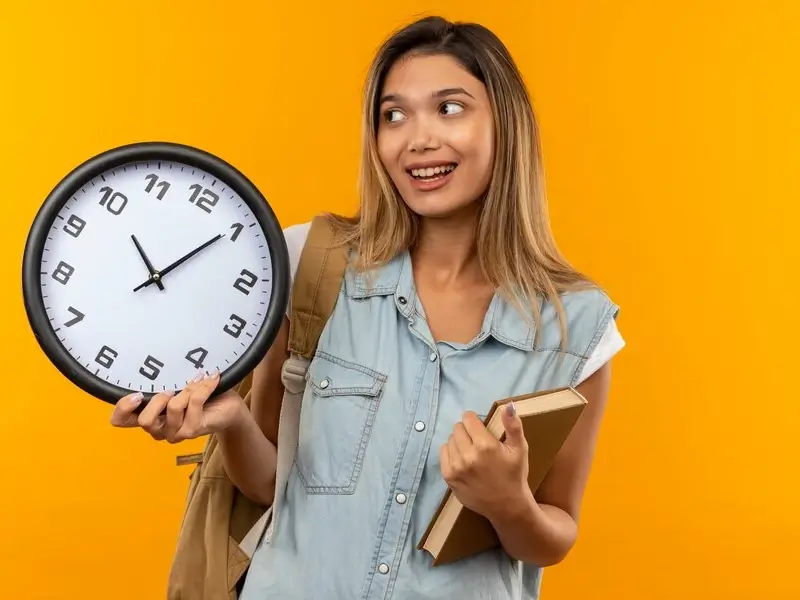 Relógio sobre uma mesa de estudos com agenda e material escolar